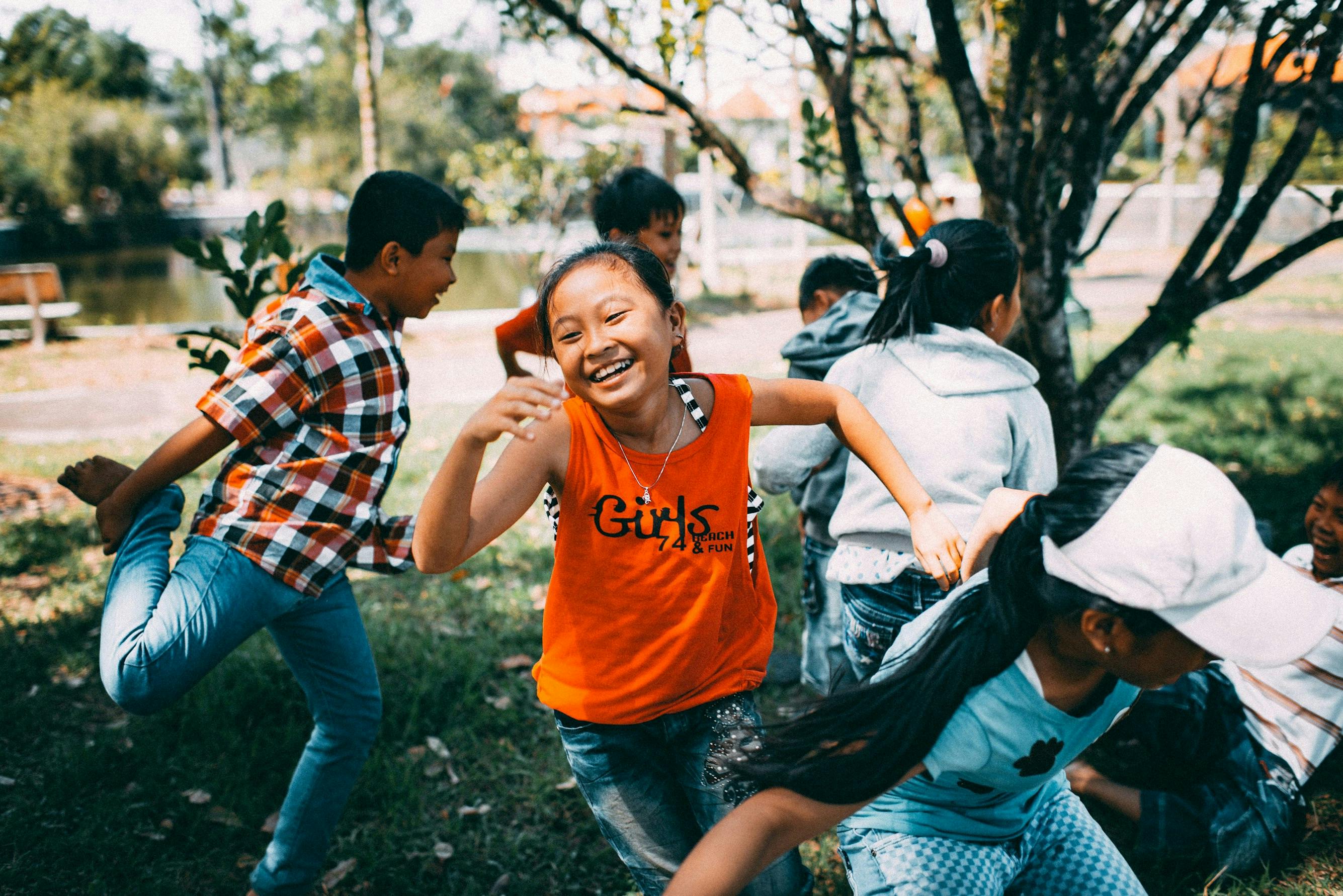 Girl in orange t-shirt playing game with group of kids in park